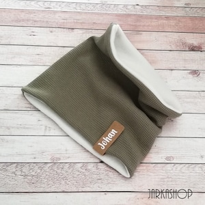 Könnte beinhalten: Ein grüner und weißer Fleece-Halswärmer mit einem braunen Etikett, auf dem "Johan" steht.