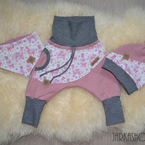 以下が含まれることがあります： ラマ柄のピンクのベビー服セット。セットには、グレーのウエストバンドが付いたパンツ、それに合わせた帽子、よだれかけが含まれています。