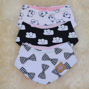 May include: Three reversible baby bibs with different patterns. The top bib has a white background with black sheep, the middle bib has a black background with white clouds, and the bottom bib has a white background with black bow ties.