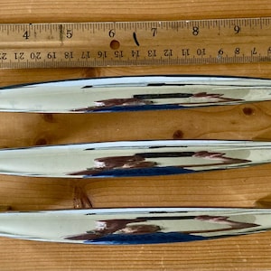 May include: Three shiny, silver-colored, elongated decorative objects are displayed on a wooden surface next to a ruler. The objects are approximately 10 inches long. The ruler is marked with inches and numbers.