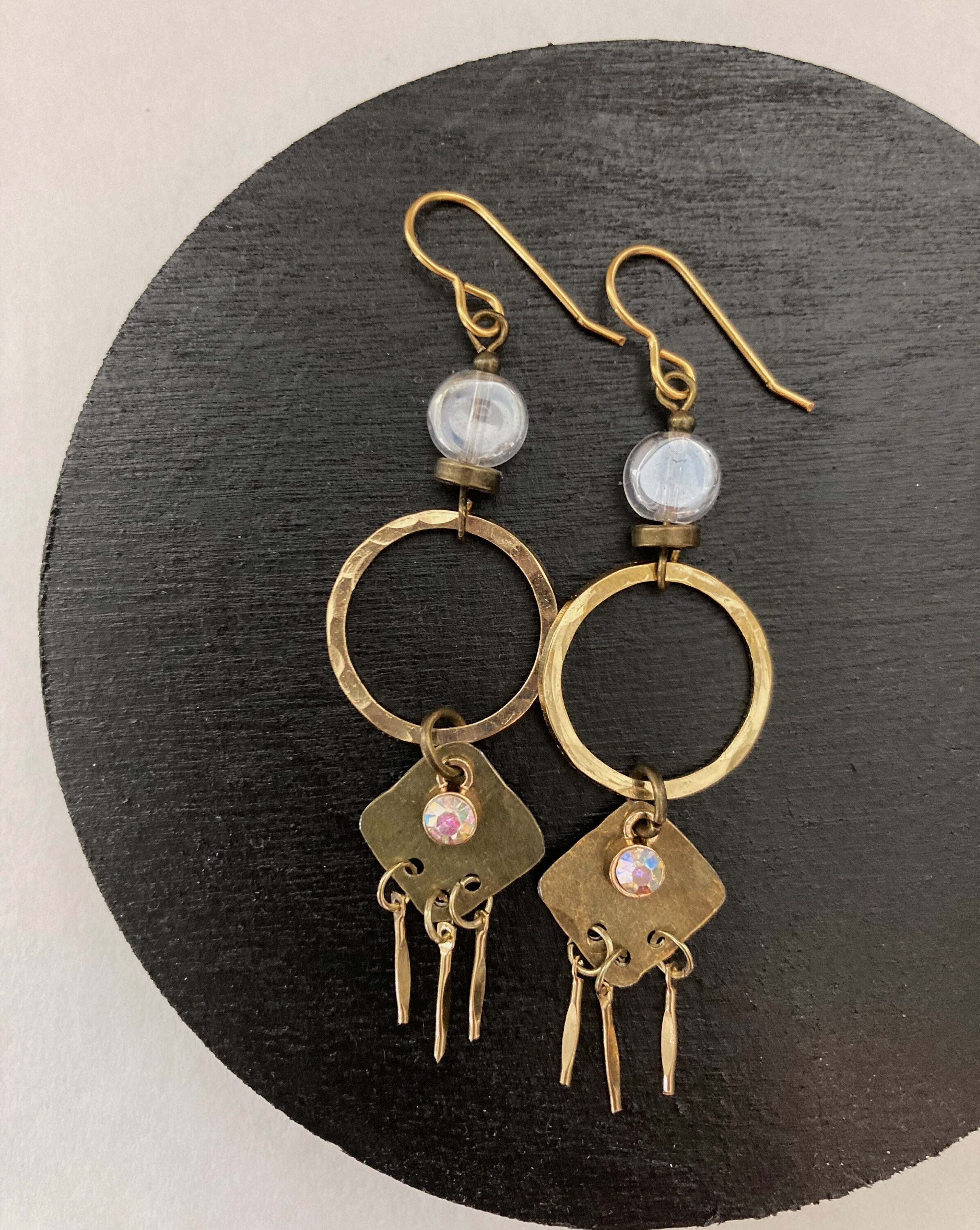 Boho Chic defines this shimmering silhouette in hammered gold + brass. Golden icicles dangle from a textured hoop adorned w/ a clear agate.