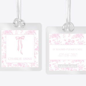 May include: Two square luggage tags with clear plastic loops. The tags feature a pink floral pattern, a pink bow illustration, and the text CHARLIE ANNE. The reverse side displays the text IF FOUND PLEASE CALL: 123-456-7890 and THE SOUTHERN PEN & POST.