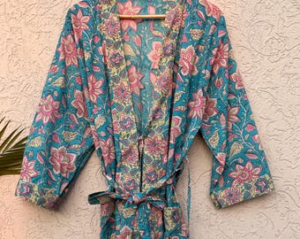May include: A turquoise floral print robe with a matching belt, hanging on a wooden hanger. The robe features a vibrant pattern of pink and yellow flowers and leaves. The robe is approximately 55 inches long.