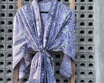 May include: A purple and white floral print robe with a dark blue trim. The robe has a tie belt and a pocket on the left side.