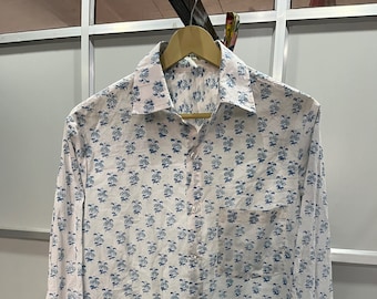 May include: A white long-sleeved button-down shirt with a blue floral print. The shirt has a pocket on the left side and a button-up collar.