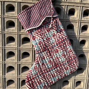 以下が含まれることがあります： 幾何学模様の赤いキルティングのクリスマスストッキング。ストッキングは白いトリムと青と赤のストライプのカフスが付いています。