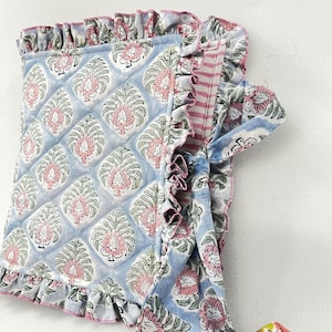 Könnte beinhalten: Hellblaues, gestepptes Gewebe mit einem Blumenmuster in Rosa und Grün. Der Stoff hat einen Rüschenrand und eine passende Krawatte. Das Design ist ein sich wiederholendes Blumenmotiv. Das Gesamtthema ist ein floraler Textil.
