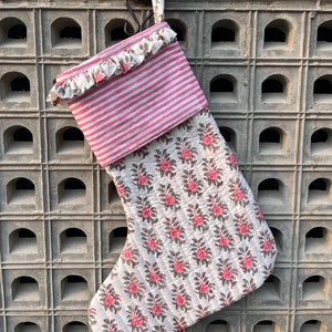 May include: A white and pink Christmas stocking with a floral print and a pink and white striped cuff. The stocking has a ruffled edge and is hanging from a hook.