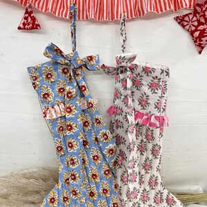 Puede incluir: Dos calcetines navideños con estampados florales. Uno es azul claro con flores rojas y amarillas, el otro es blanco con flores rosas. Ambos tienen volantes y lazos. Una guirnalda a rayas rojas y blancas cuelga encima.