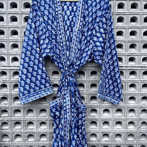 May include: A blue floral print robe with long sleeves and a tie waist. The robe is made of a lightweight fabric and features a white floral pattern. The robe is hanging on a wooden hanger against a textured wall.