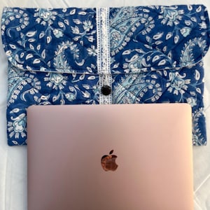 May include: A rose gold laptop computer with an Apple logo on the lid. The laptop is sitting on a white surface and is inside a blue and white paisley patterned laptop sleeve.