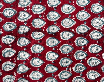May include: Red fabric with a repeating pattern of white and blue teardrop shapes. The teardrop shapes have a geometric design inside.