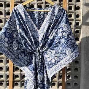 May include: A blue and white cotton kaftan with a floral print. The kaftan has a V-neck and a tie at the waist.