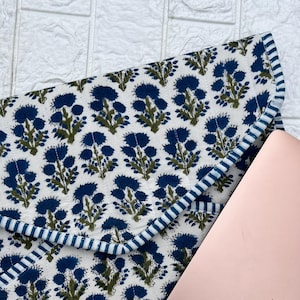 May include: A blue and green floral patterned laptop sleeve with a white background and a blue and white striped trim. The sleeve is folded over a rose gold laptop.