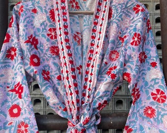May include: A floral print robe in shades of lavender, red, and teal, hanging on a wooden hanger. The robe features a tie closure and wide sleeves. The pattern includes stylized flowers and leaves.