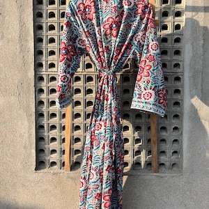 May include: A long, blue and red floral print robe with a tie belt. The robe is hanging on a wooden rack against a gray wall.