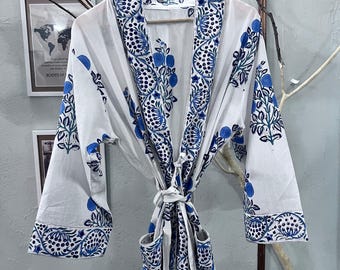 May include: White robe with a blue floral pattern, hanging on a wooden hanger. The robe features a tie closure and pockets. The sleeves and edges are trimmed with a detailed blue design. The robe is made of a lightweight fabric.