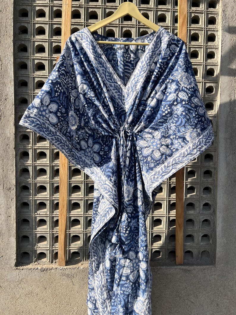 Puede incluir: Una kaftan de algod&oacute;n azul y blanco con estampado floral. La kaftan tiene cuello en V y un lazo en la cintura.