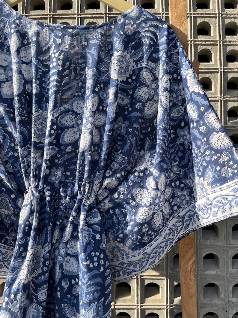 Puede incluir: Una kaftan de algod&oacute;n con estampado floral azul y blanco, con cintura fruncida y un borde alrededor de los bordes.