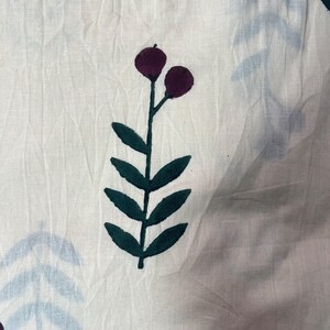 May include: White fabric with a repeating pattern of stylized botanical elements. The design features dark purple berries and dark green leaves on stems, with light blue leaf shapes scattered across the surface. The fabric has a slightly wrinkled texture.
