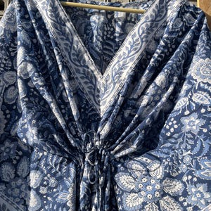 Puede incluir: Una kaft&aacute;n de algod&oacute;n azul y blanco con estampado floral y cuello en V. La kaft&aacute;n tiene una cintura con cord&oacute;n y un ajuste holgado.