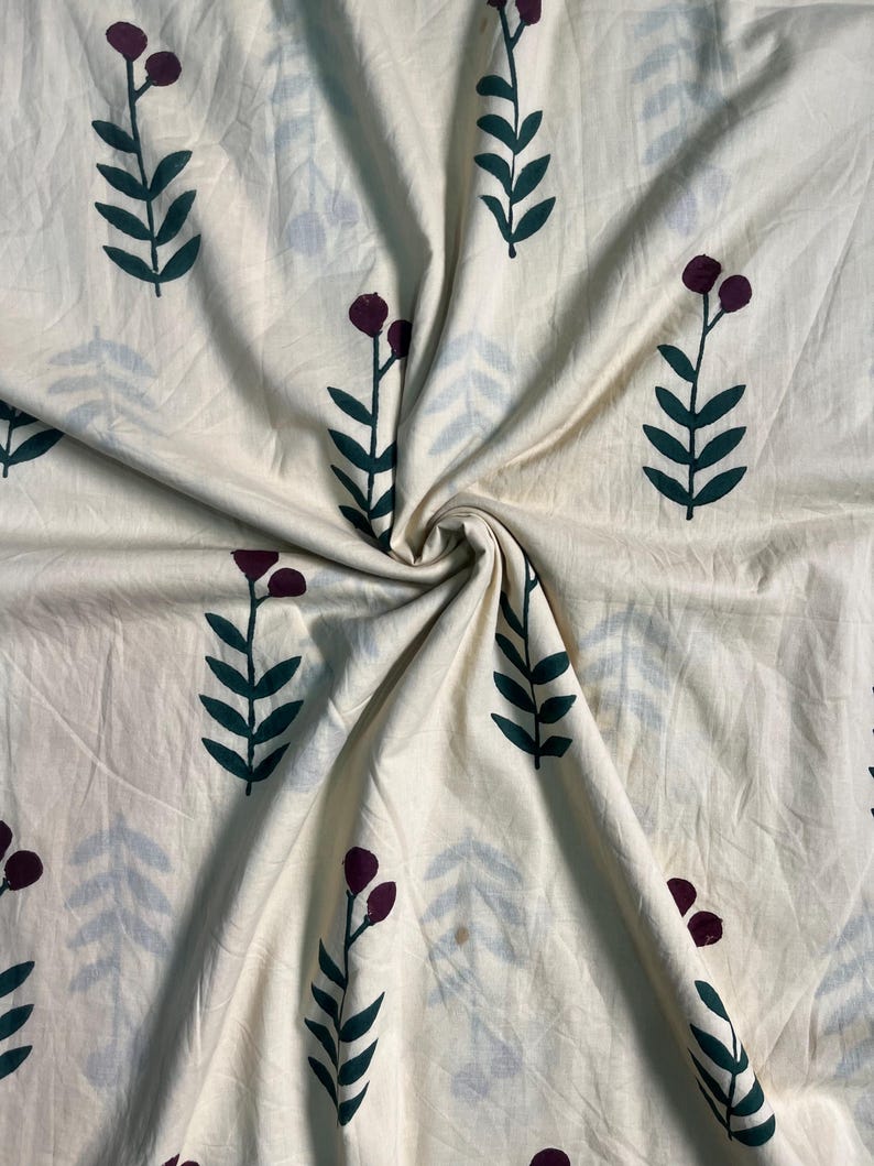 May include: Cream-colored fabric with a repeating pattern of dark green leaves and burgundy berry clusters on stems. Faint blue-gray leaf shapes are also scattered across the fabric. The fabric is gathered and folded, showing its texture.