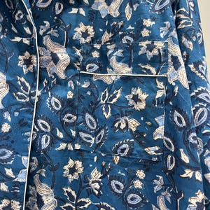 May include: A teal blue cotton shirt with a white floral pattern. The shirt has a button-up front and a pocket on the left side.