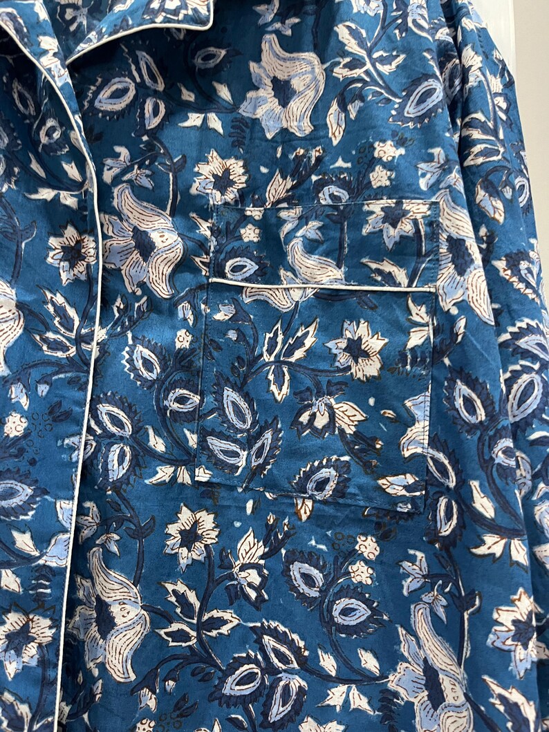 May include: A teal blue cotton shirt with a white floral pattern. The shirt has a button-up front and a pocket on the left side.