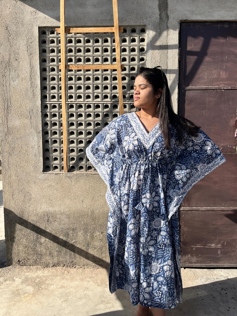 Puede incluir: Una kaft&aacute;n de estampado floral azul y blanco con cuello en V y mangas largas. La kaft&aacute;n tiene una cintura con cord&oacute;n y una silueta fluida.