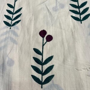 May include: Off-white fabric with a repeating pattern of stylized floral elements. Dark green leaves and stems support clusters of two deep purple berries. The design is printed on a slightly wrinkled, textured material.
