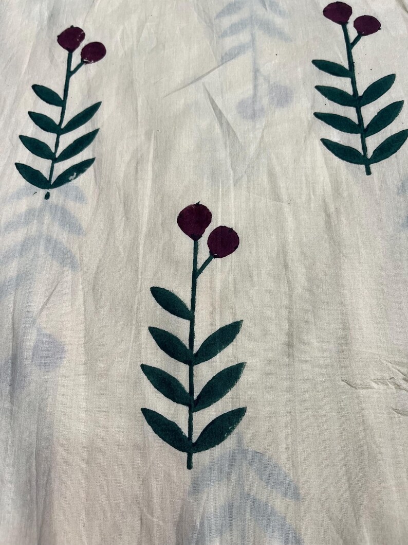May include: Off-white fabric with a repeating pattern of stylized floral elements. Dark green leaves and stems support clusters of two deep purple berries. The design is printed on a slightly wrinkled, textured material.