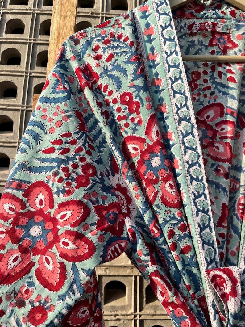 May include: A blue and red floral print cotton robe with a white trim. The robe has a long sleeve and a tie closure.