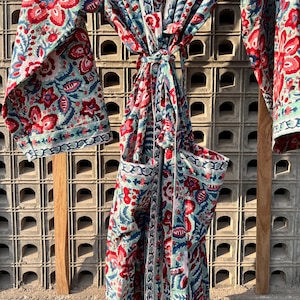May include: A long, blue and red floral print robe with a tie belt. The robe has a pocket on the left side.