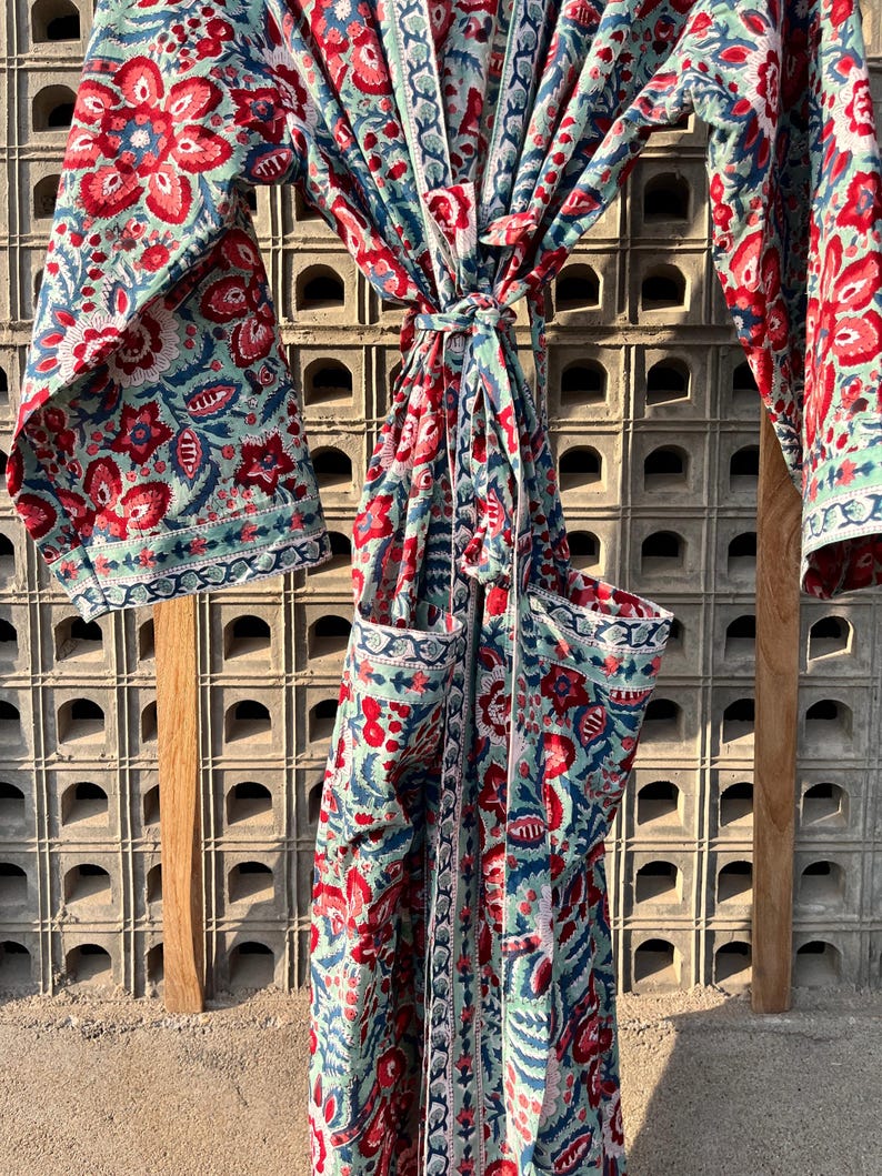 May include: A long, blue and red floral print robe with a tie belt. The robe has a pocket on the left side.