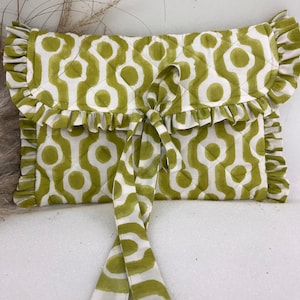May include: A quilted clutch with a white and olive green geometric pattern. The clutch has a ruffled edge and a matching tie closure. The design features a repeating pattern of interconnected shapes, creating a stylish accessory.