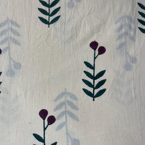 May include: Cream-colored fabric with a repeating pattern of stylized floral elements. Dark green leaves and stems support clusters of two or three deep purple berries. Faint blue-gray leaf shapes are also scattered across the fabric.