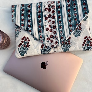 May include: A white quilted laptop sleeve with a floral pattern in shades of red, green, and blue. The sleeve is folded over a rose gold laptop.