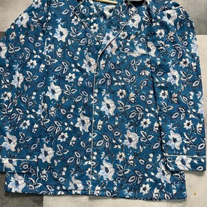May include: A teal blue long-sleeved shirt with a white floral print. The shirt has a button-up front and a collar.
