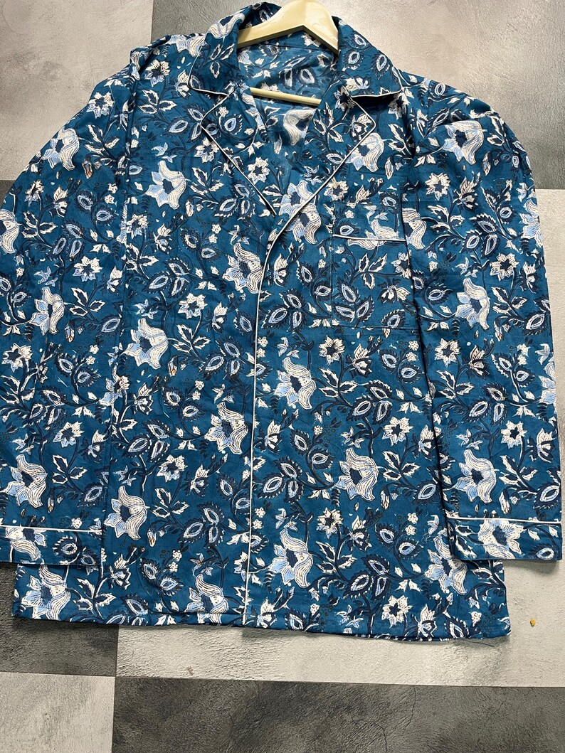 May include: A teal blue long-sleeved shirt with a white floral print. The shirt has a button-up front and a collar.