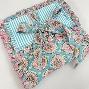 Peut inclure: Un article en tissu matelassé rectangulaire présentant une section à rayures bleues et blanches et un motif floral bleu avec des détails roses et verts. La pièce est finie avec un bord à volants bordé de rose et un lien en tissu assorti.