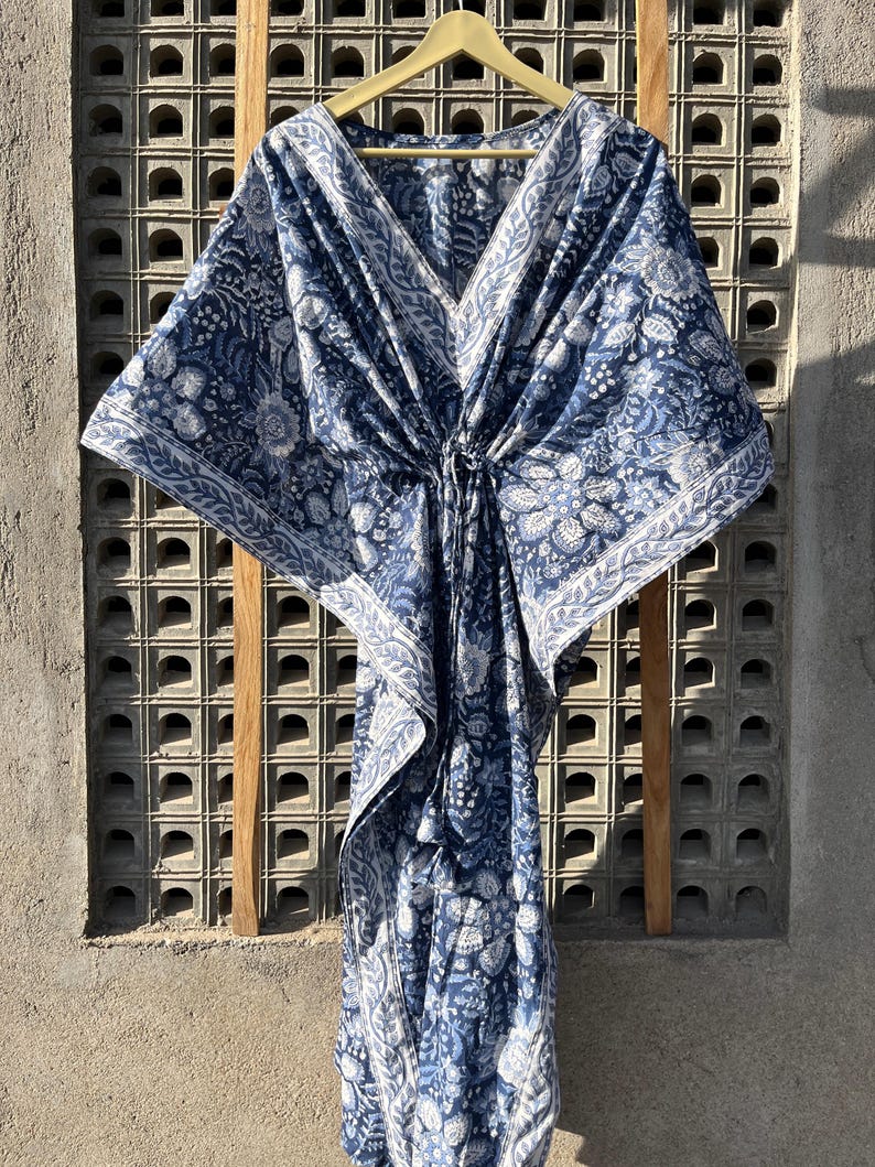 Puede incluir: Una kaft&aacute;n de algod&oacute;n azul y blanco con estampado floral. La kaft&aacute;n tiene cuello en V y un lazo en la cintura.