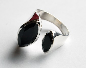 May include: A silver-toned ring with two black, teardrop-shaped stones. The ring band curves around the finger, with the stones positioned on either side. The ring has a modern, minimalist design, and the stones have a faceted appearance.