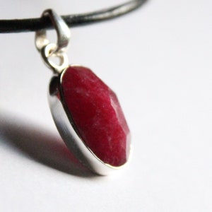 Può includere: Una collana con un ciondolo d'argento e una grande pietra rossa sfaccettata.