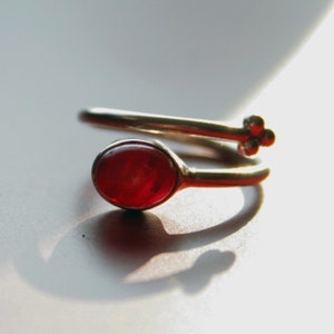Könnte beinhalten: Ein silberner Ring mit einem roten Edelstein in der Mitte. Der Ring ist so konzipiert, dass er sich um den Finger wickelt.