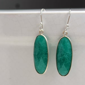 Può includere: Un paio di orecchini pendenti in argento con pietre preziose verdi di forma ovale. Le pietre preziose sono tagliate a faccette e sono incastonate in una montatura in argento.
