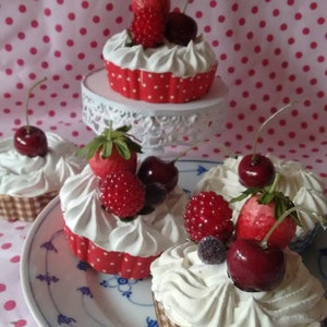 Könnte beinhalten: Ein Set aus sechs Cupcakes, die mit weißem Frosting und roten und weißen Streuseln verziert sind. Jeder Cupcake ist mit einer Auswahl an frischen Früchten belegt, darunter Erdbeeren, Kirschen und Blaubeeren. Die Cupcakes sind auf einem weißen Teller mit einem blauen und weißen Muster angeordnet.