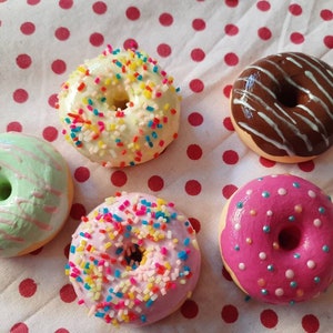 Könnte beinhalten: Fünf bunte Donuts mit verschiedenen Toppings. Ein grüner Donut mit rosa Zuckerguss, ein weißer Donut mit gelben und rosa Streuseln, ein brauner Donut mit weißen Streifen, ein rosa Donut mit weißen und blauen Streuseln und ein rosa Donut mit weißen und blauen Streuseln.