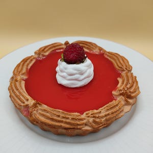 Könnte beinhalten: Eine rote Obsttorte mit einem weißen Baiser-Topping und einer einzelnen roten Beere darauf. Die Torte befindet sich auf einem weißen Teller.