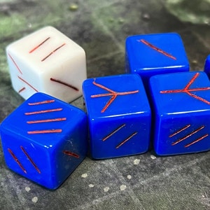 May include: Six dice with red markings on a green surface. One die is white with red markings, the other five are blue with red markings.