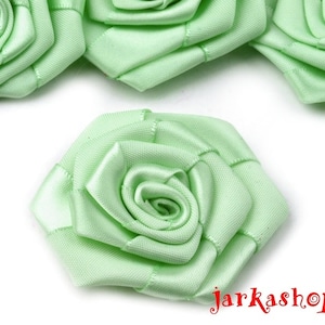 Könnte beinhalten: Nahaufnahme einer hellgrünen Satinrosenverzierung. Die Rose ist aus Stoff gefertigt und hat ein zartes, geschichtetes Design.